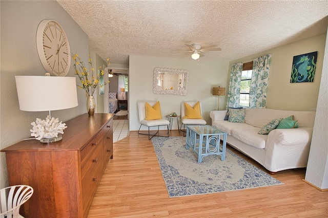 living room with ceiling fan, light hardwood / wood-style floors, and a textured ceiling