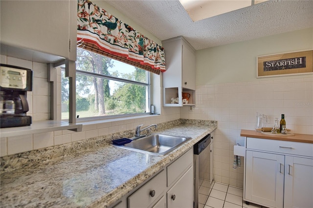 kitchen with stainless steel dishwasher, a textured ceiling, sink, white cabinetry, and light tile patterned flooring