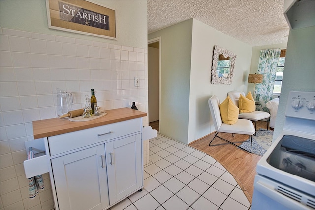 kitchen featuring white stove, white cabinets, light wood-type flooring, tile walls, and butcher block countertops