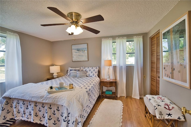 bedroom with a textured ceiling, light wood-type flooring, a closet, and ceiling fan