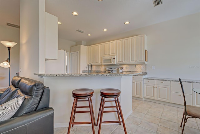 kitchen featuring decorative backsplash, light stone countertops, white appliances, and light tile patterned flooring