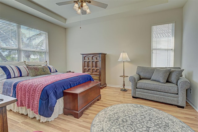 bedroom featuring ceiling fan, light hardwood / wood-style floors, and a raised ceiling