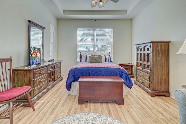 bedroom with ceiling fan, light hardwood / wood-style floors, and a tray ceiling