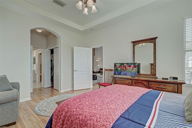 bedroom with connected bathroom, ceiling fan, a raised ceiling, and light hardwood / wood-style floors