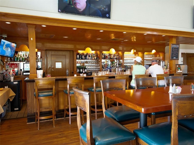 bar featuring hardwood / wood-style flooring, wood walls, ornate columns, and wooden ceiling