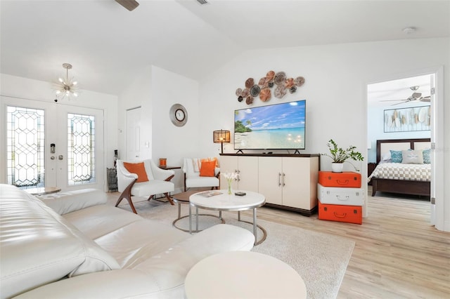 living room with french doors, ceiling fan with notable chandelier, vaulted ceiling, and light wood-type flooring