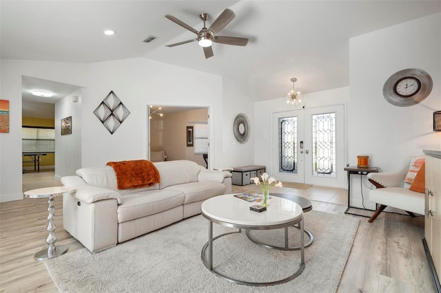 living room with ceiling fan with notable chandelier, french doors, light wood-type flooring, and vaulted ceiling