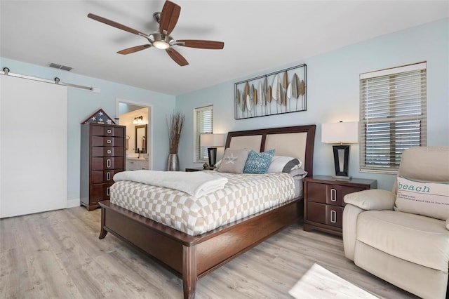 bedroom with connected bathroom, ceiling fan, light hardwood / wood-style floors, and a barn door