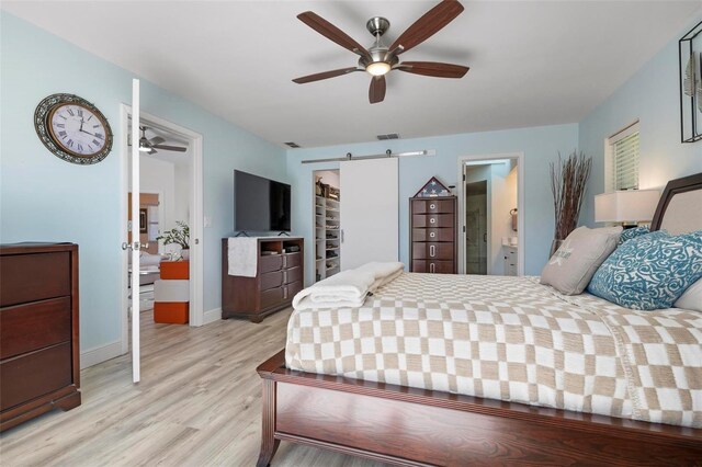 bedroom featuring a barn door, ensuite bathroom, ceiling fan, and light hardwood / wood-style floors