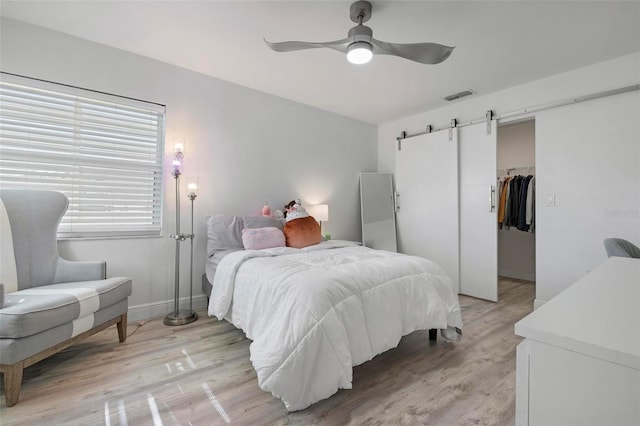 bedroom with a closet, ceiling fan, light hardwood / wood-style flooring, and a barn door