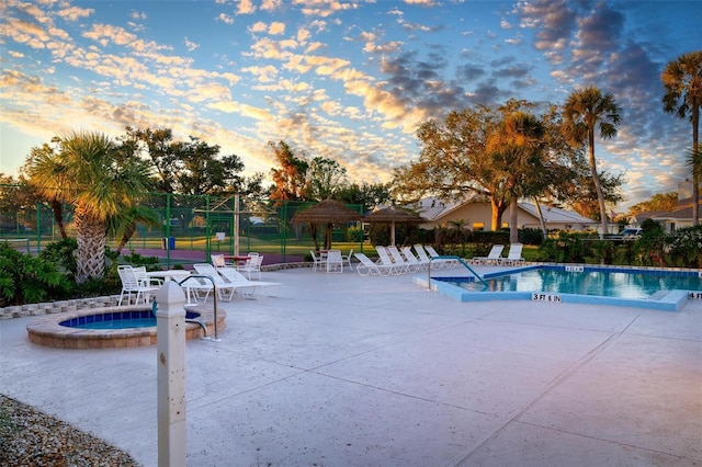 pool at dusk featuring a community hot tub and a patio