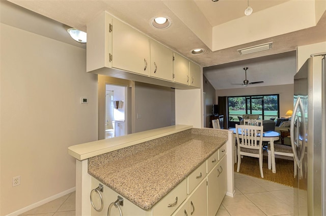 kitchen with ceiling fan, light stone countertops, light tile patterned floors, kitchen peninsula, and stainless steel refrigerator