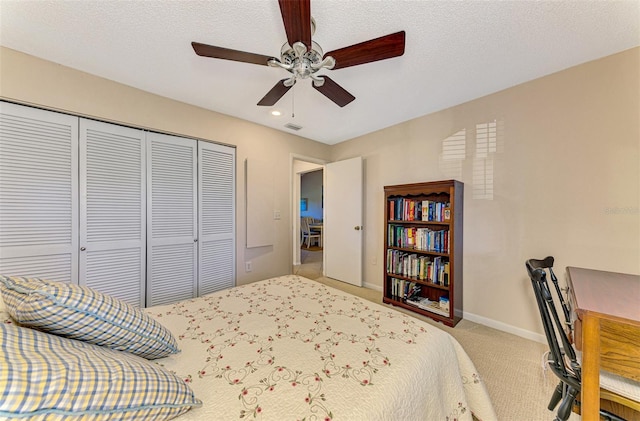 bedroom featuring ceiling fan, a closet, light colored carpet, and a textured ceiling