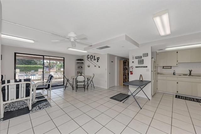 kitchen featuring white refrigerator, sink, ceiling fan, light tile patterned floors, and cream cabinetry