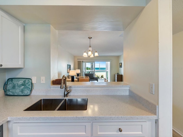 kitchen with white cabinets, light stone counters, sink, and a chandelier