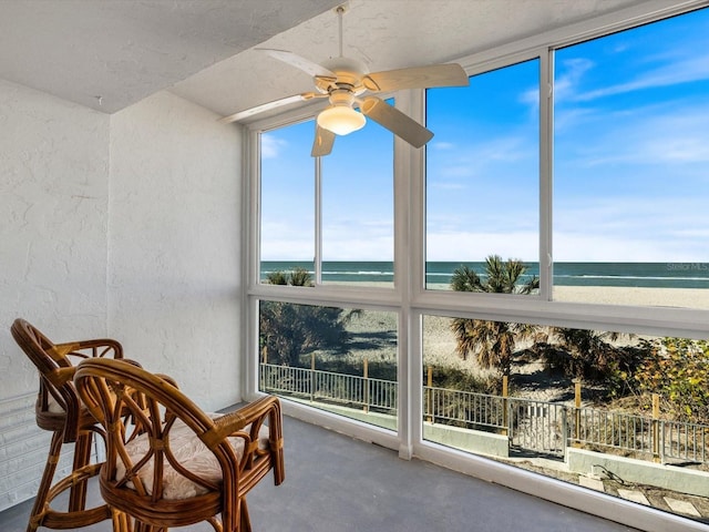 sunroom featuring ceiling fan, a water view, and a beach view