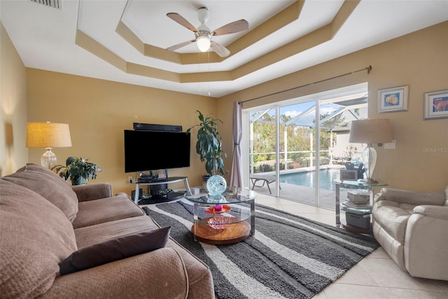 living room with ceiling fan, light tile patterned flooring, and a tray ceiling