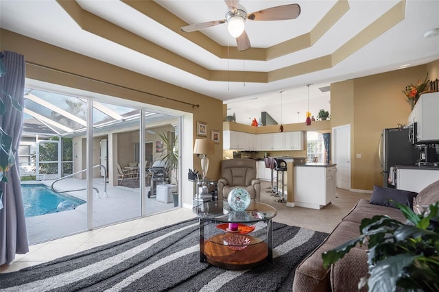 tiled living room with a tray ceiling and ceiling fan