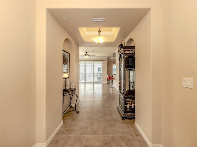 corridor with a raised ceiling and light tile patterned floors