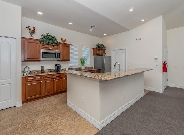 kitchen with sink, stainless steel appliances, light stone counters, an island with sink, and light colored carpet