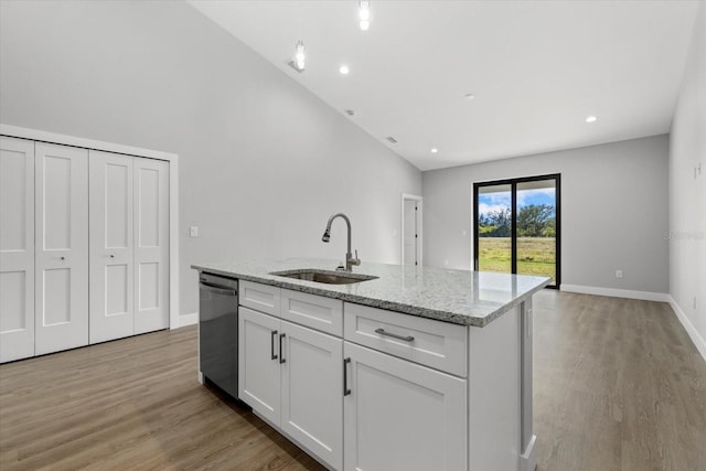 kitchen featuring a center island with sink, light stone counters, stainless steel dishwasher, sink, and white cabinetry