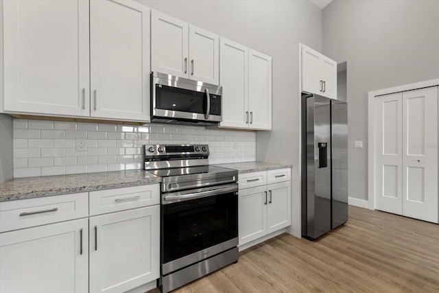 kitchen with white cabinetry, light stone countertops, stainless steel appliances, and light hardwood / wood-style flooring