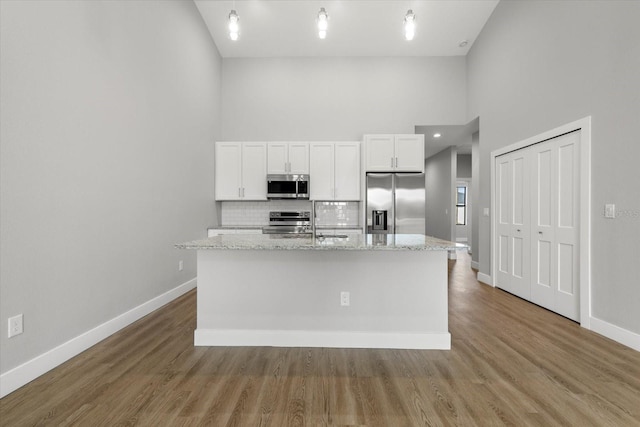 kitchen with white cabinets, appliances with stainless steel finishes, light stone counters, and a kitchen island with sink