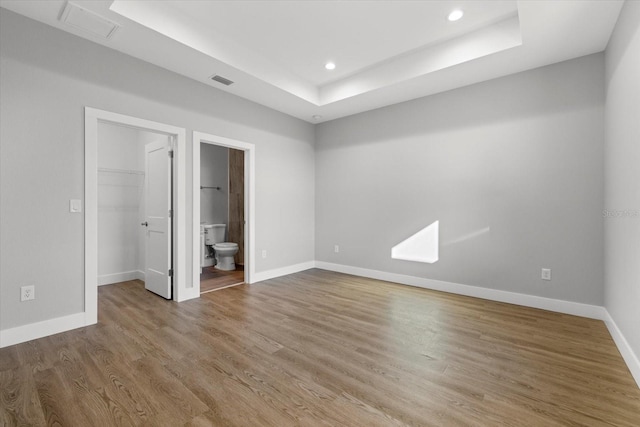 unfurnished bedroom with a closet, a walk in closet, wood-type flooring, connected bathroom, and a raised ceiling