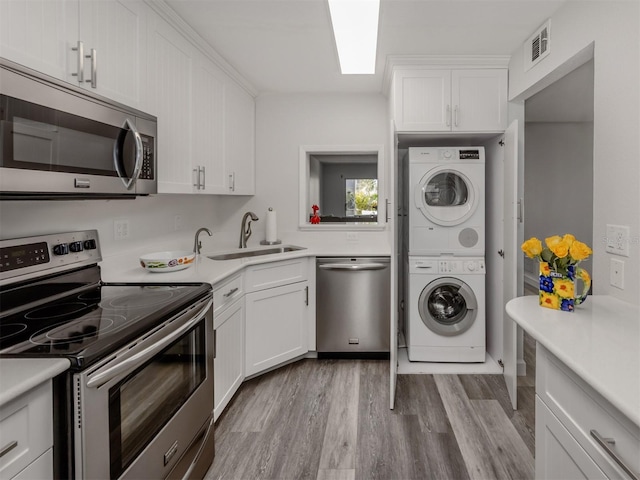 kitchen with white cabinets, sink, stacked washer and dryer, and stainless steel appliances