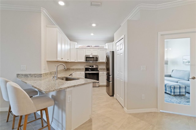 kitchen with white cabinets, crown molding, sink, appliances with stainless steel finishes, and a breakfast bar area