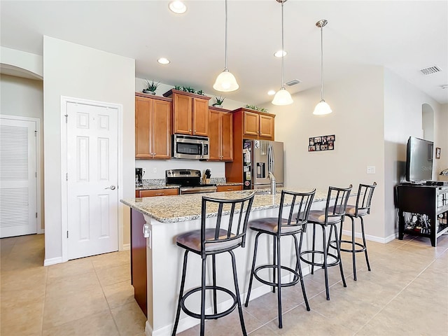 kitchen featuring light stone counters, stainless steel appliances, pendant lighting, a center island with sink, and a breakfast bar area