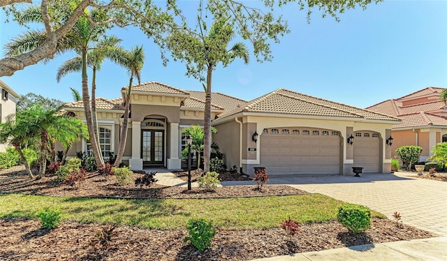 mediterranean / spanish-style house featuring decorative driveway, french doors, a tile roof, stucco siding, and a garage