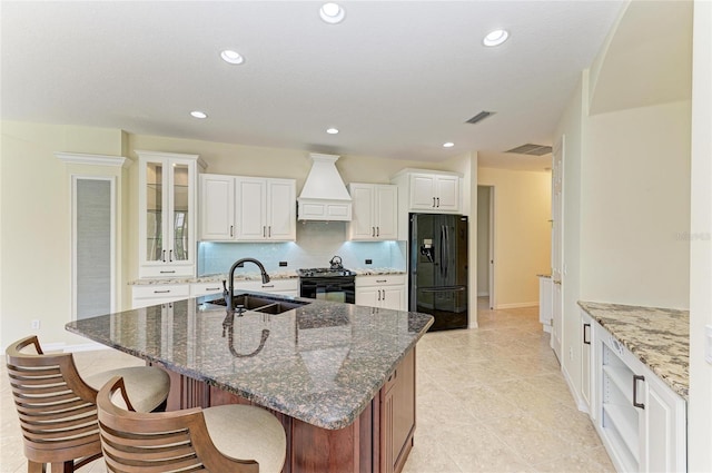 kitchen featuring premium range hood, a sink, visible vents, decorative backsplash, and black appliances