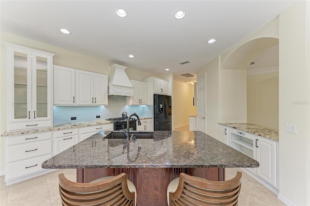 kitchen featuring a sink, a kitchen bar, custom range hood, and black fridge