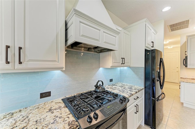 kitchen featuring premium range hood, visible vents, white cabinetry, black refrigerator with ice dispenser, and gas stove