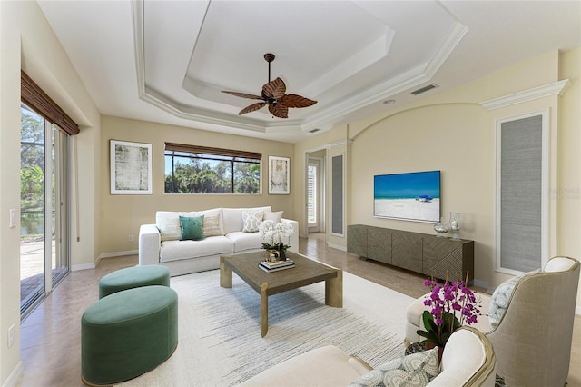 living room with a raised ceiling, visible vents, ceiling fan, and baseboards