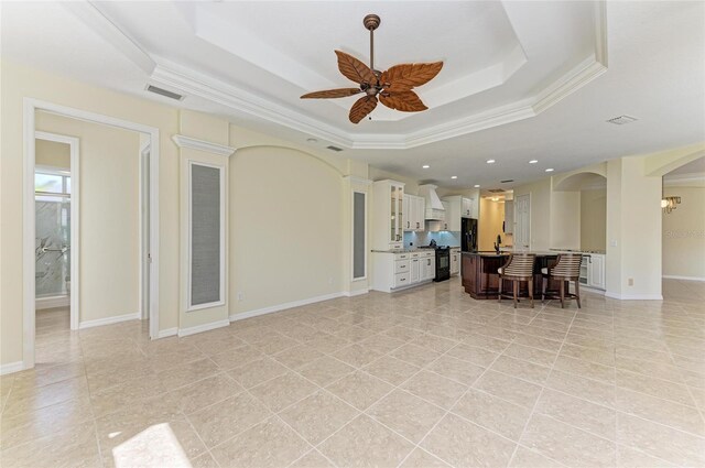 living room featuring visible vents, arched walkways, a ceiling fan, a tray ceiling, and crown molding