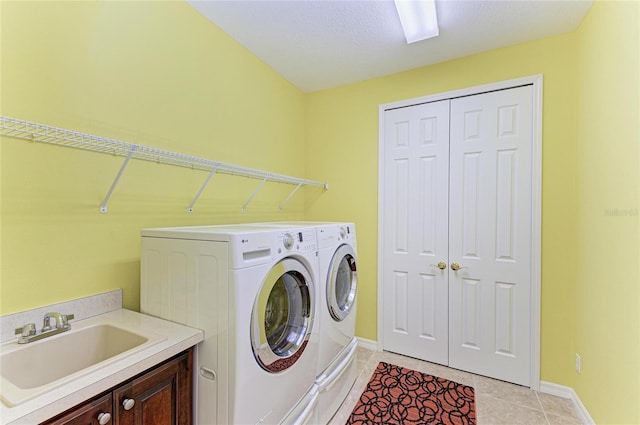 clothes washing area with light tile patterned floors, cabinet space, baseboards, washing machine and dryer, and a sink