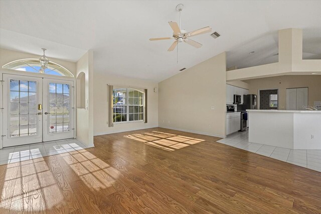 unfurnished living room with french doors, light hardwood / wood-style floors, vaulted ceiling, and ceiling fan