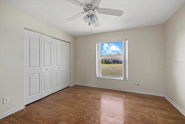 unfurnished bedroom with ceiling fan, a closet, and dark wood-type flooring