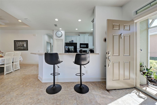 kitchen featuring light tile patterned floors, kitchen peninsula, a kitchen bar, white cabinets, and black appliances