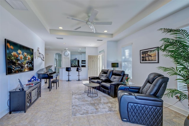 living room featuring a raised ceiling, ceiling fan, and light tile patterned flooring