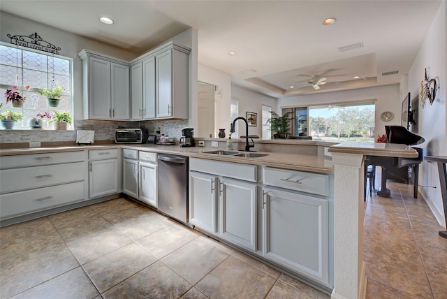 kitchen with kitchen peninsula, tasteful backsplash, a tray ceiling, ceiling fan, and sink