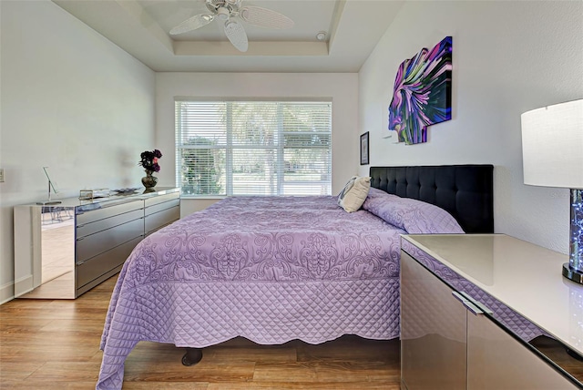 bedroom featuring a tray ceiling, ceiling fan, and light hardwood / wood-style flooring