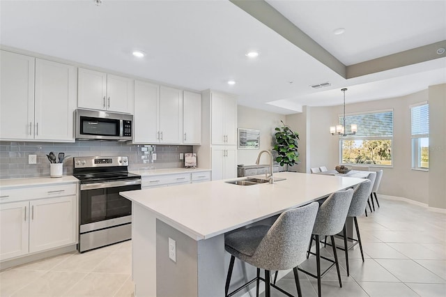 kitchen featuring stainless steel appliances, light countertops, white cabinets, a sink, and an island with sink