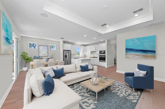 living room featuring a raised ceiling, ornamental molding, and light hardwood / wood-style flooring