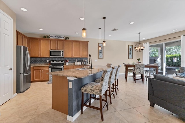 kitchen with stainless steel appliances, sink, decorative light fixtures, a chandelier, and an island with sink