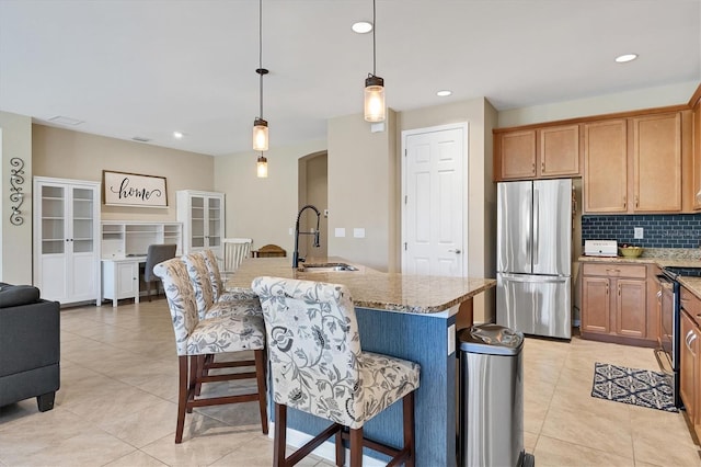 kitchen with stainless steel fridge, sink, decorative light fixtures, black range with electric stovetop, and an island with sink