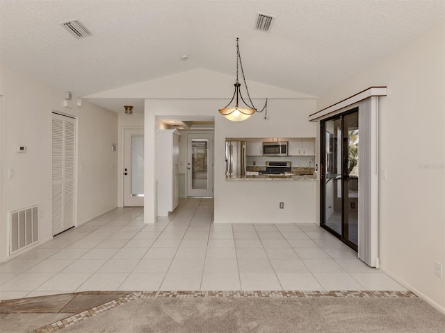 kitchen with light stone countertops, hanging light fixtures, lofted ceiling, light tile patterned flooring, and appliances with stainless steel finishes