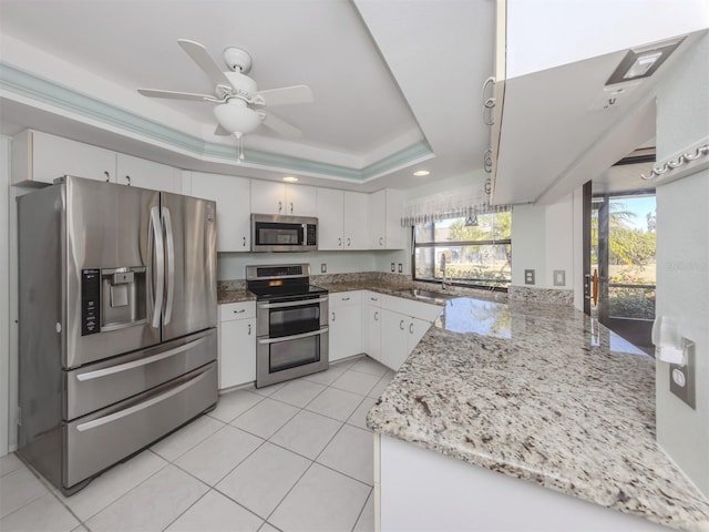 kitchen featuring white cabinetry, light stone countertops, kitchen peninsula, a tray ceiling, and appliances with stainless steel finishes